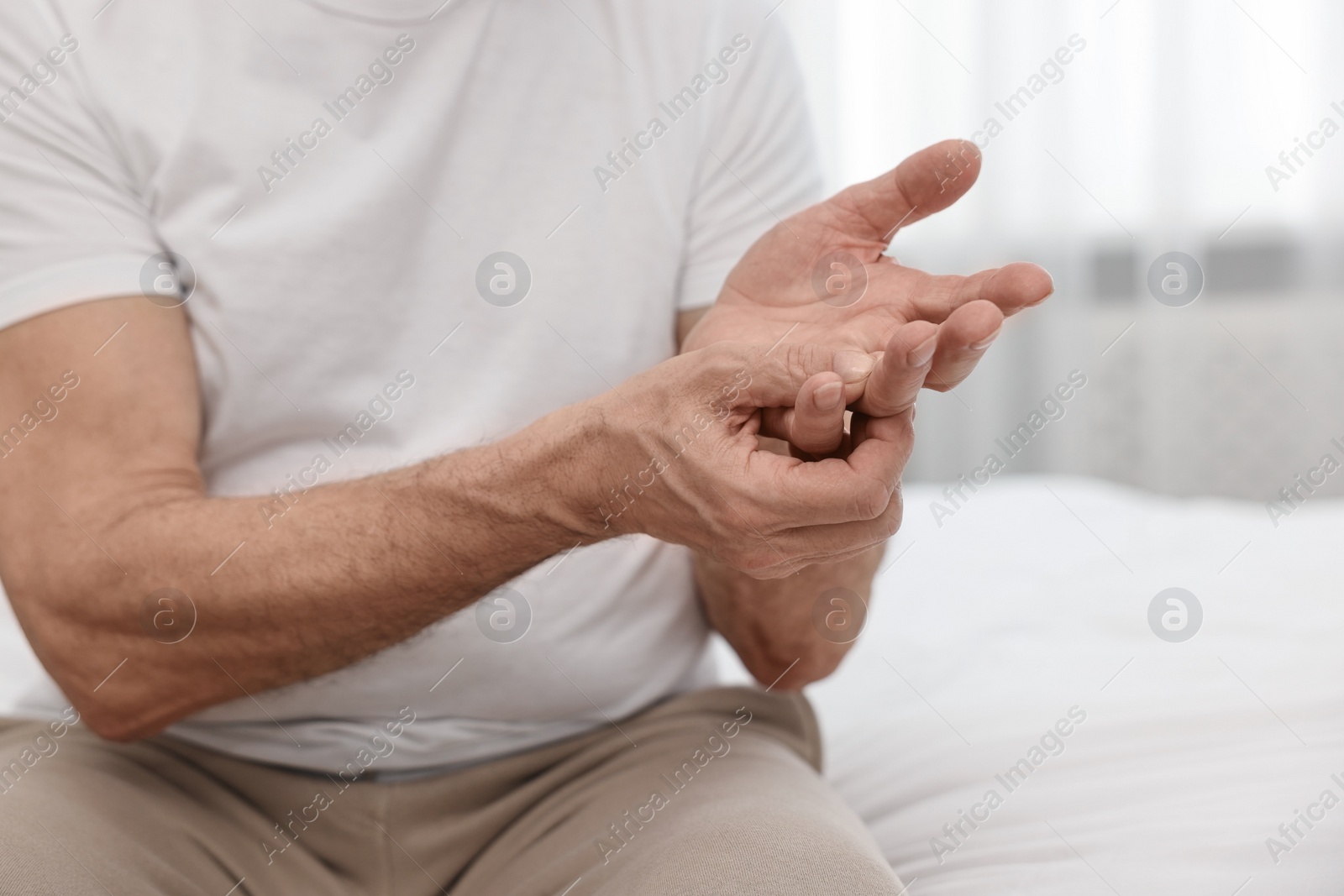 Photo of Arthritis symptoms. Man suffering from pain in hand on bed at home, closeup