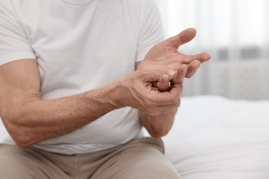 Photo of Arthritis symptoms. Man suffering from pain in hand on bed at home, closeup
