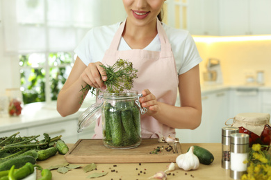 Woman putting dill into pickling jar at table in kitchen, closeup