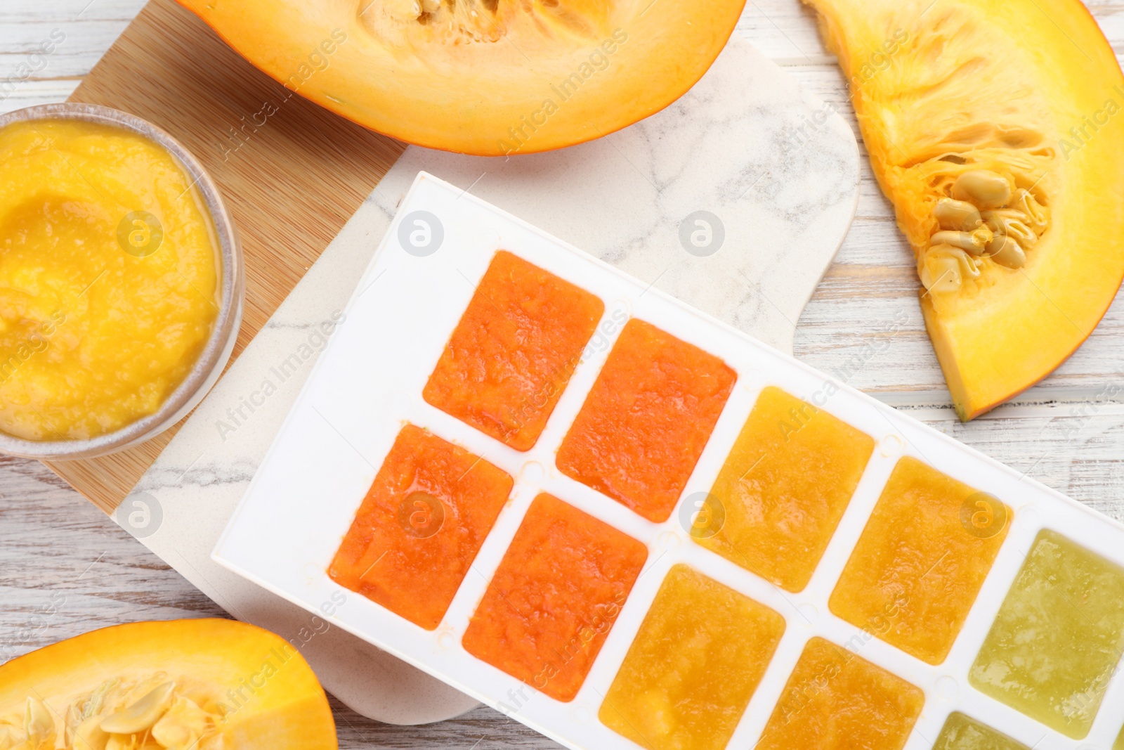 Photo of Different purees in ice cube tray and fresh pumpkin on white wooden table, flat lay. Ready for freezing