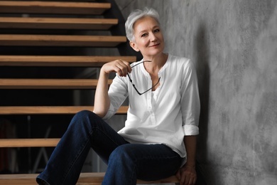 Happy mature woman sitting on wooden stairs indoors. Smart aging