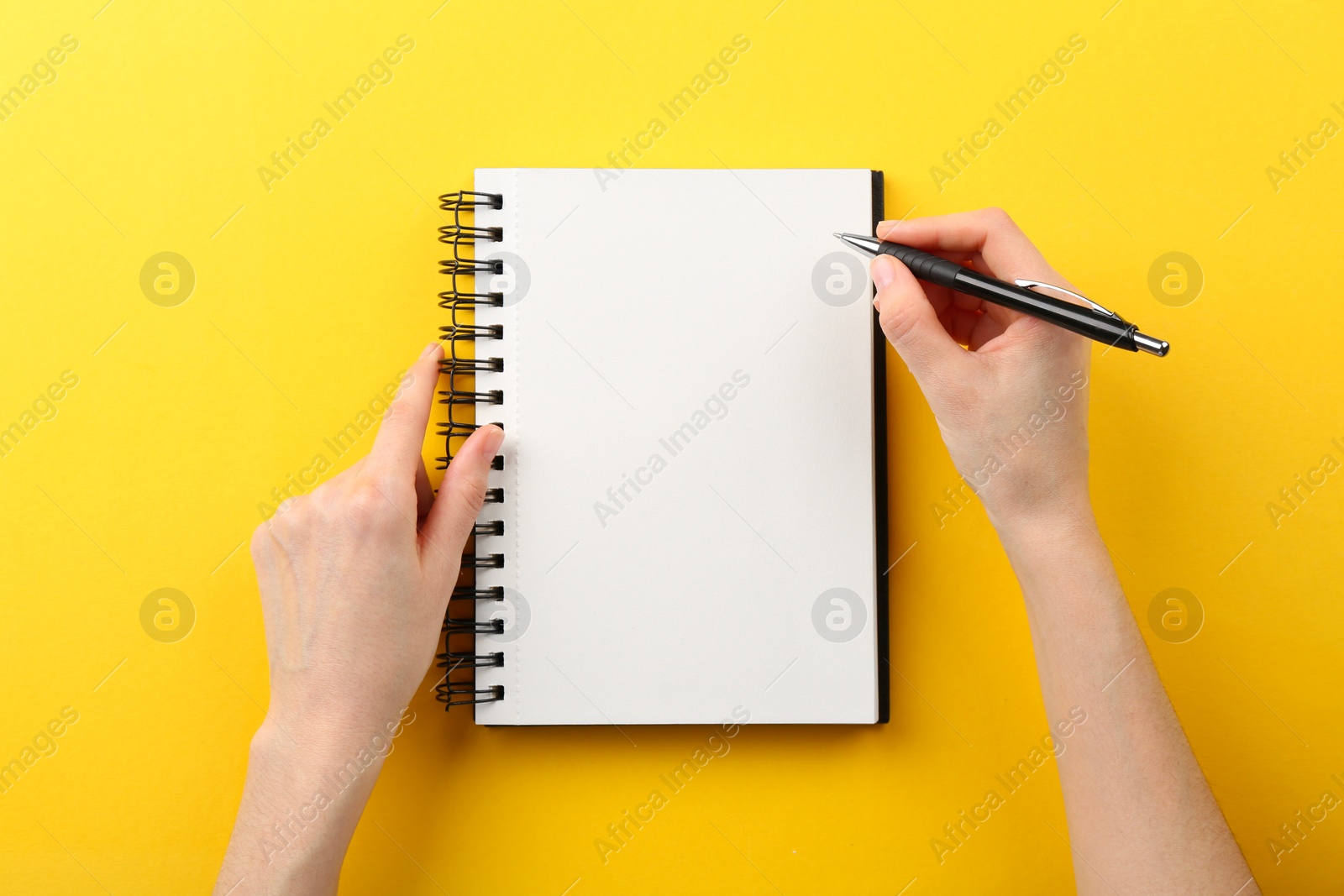 Photo of Woman writing in notebook on yellow background, top view