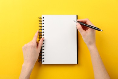 Photo of Woman writing in notebook on yellow background, top view