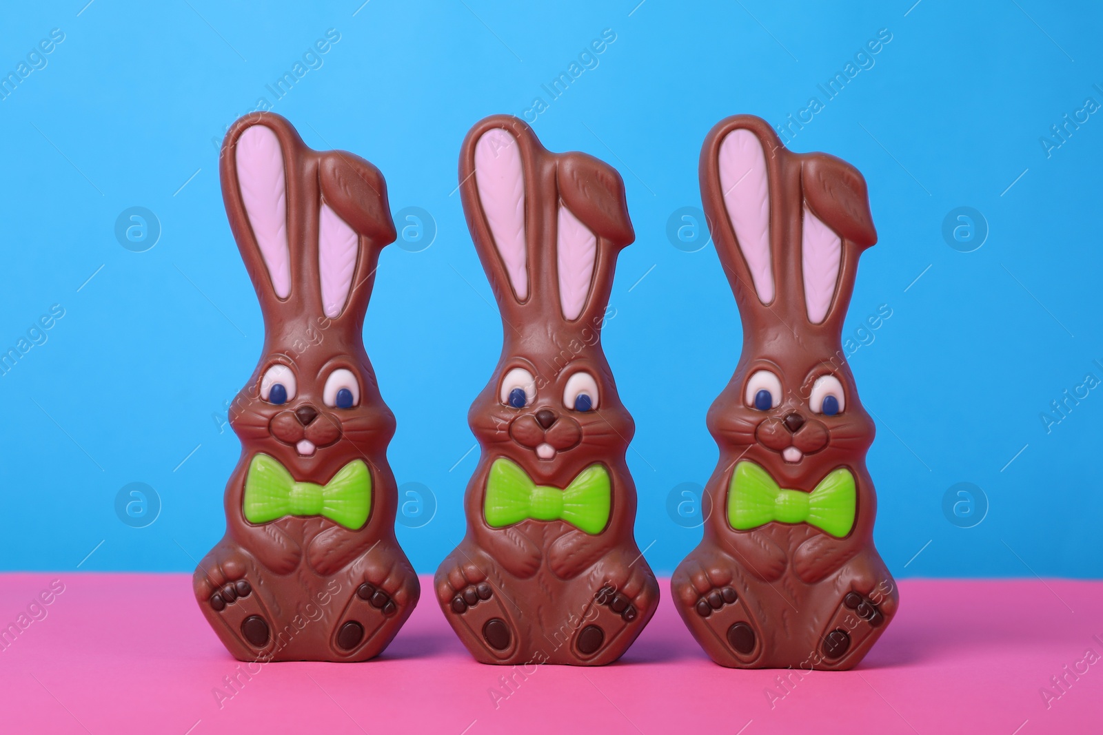 Photo of Chocolate Easter bunnies on pink table against light blue background