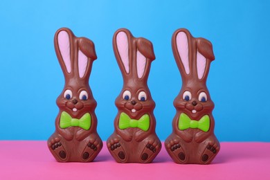 Photo of Chocolate Easter bunnies on pink table against light blue background
