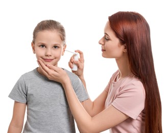 Mother spraying medication into daughter's ear on white background