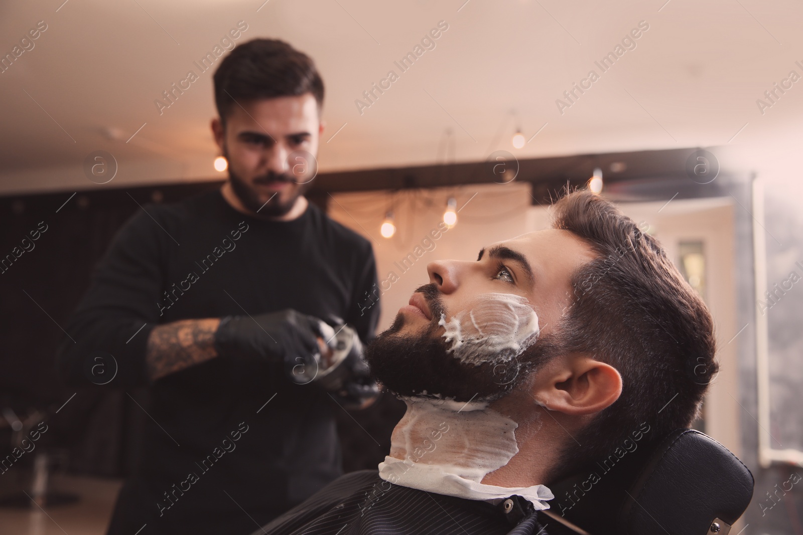 Photo of Young man with shaving foam on face in barbershop. Professional service