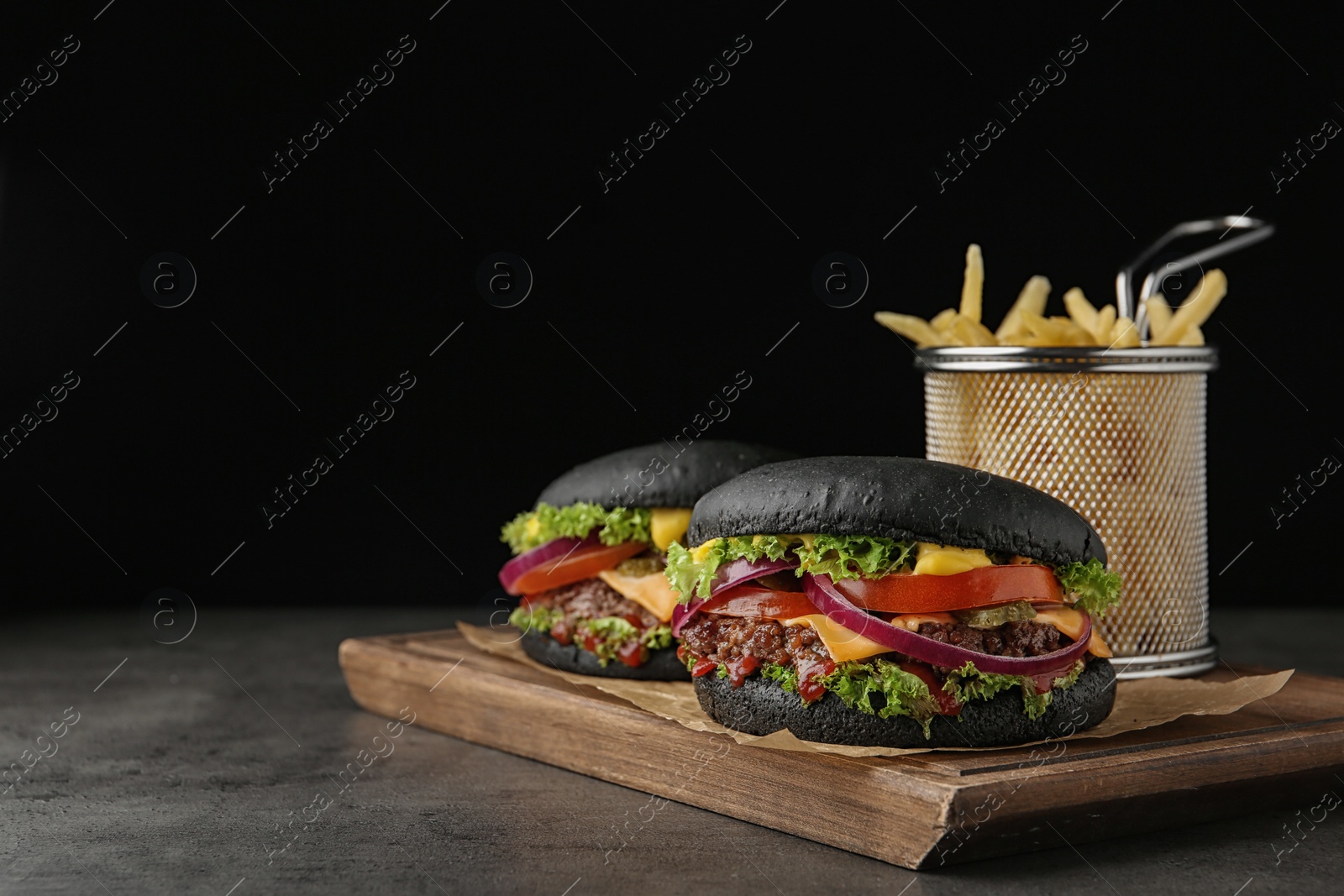 Photo of Board with black burgers and French fries on table. Space for text
