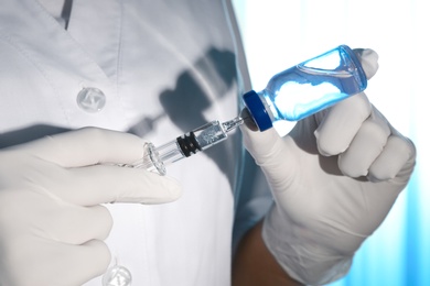 Photo of Doctor filling syringe with vaccine from vial on light background, closeup