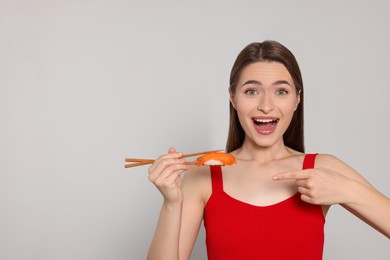 Photo of Emotional young woman holding sushi with chopsticks on light background. Space for text