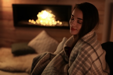 Photo of Young woman resting near decorative fireplace at home. Winter season