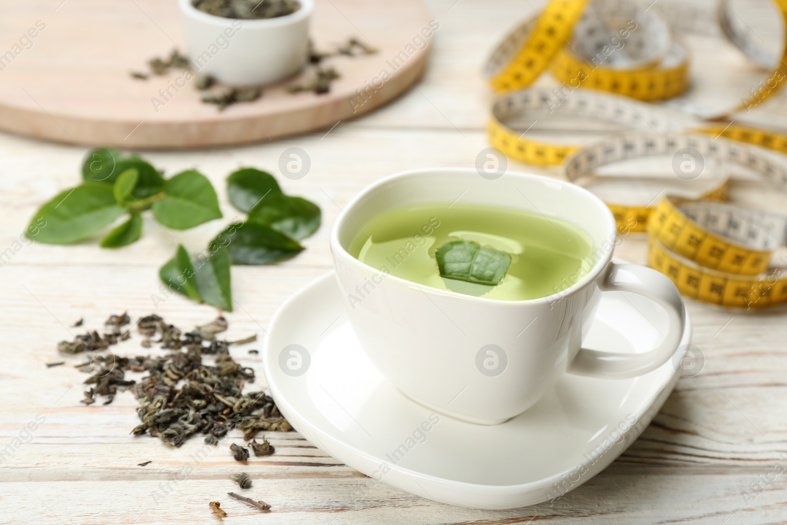 Photo of Cup of diet herbal tea and measuring tape on white wooden table