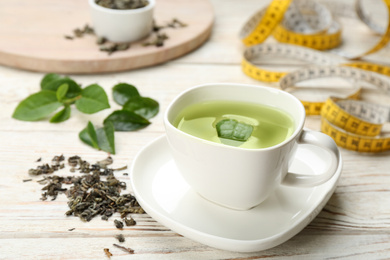 Cup of diet herbal tea and measuring tape on white wooden table