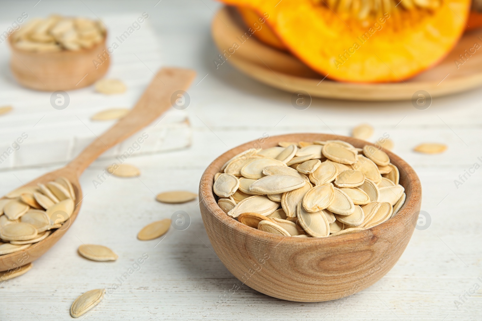 Photo of Bowl of raw pumpkin seeds on white wooden table