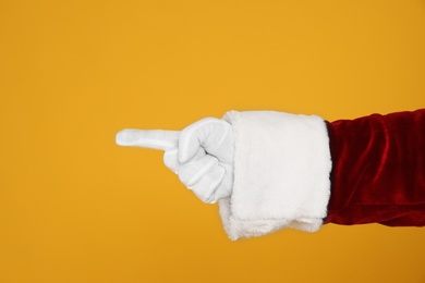 Photo of Santa Claus pointing at something on yellow background, closeup of hand