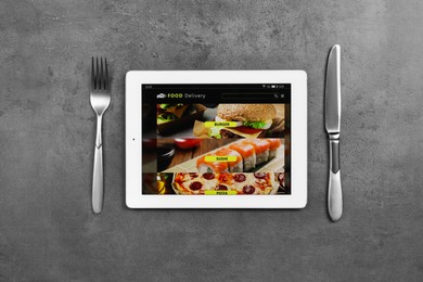 Photo of Modern tablet with open page for online food ordering and cutlery on black table, flat lay. Concept of delivery service