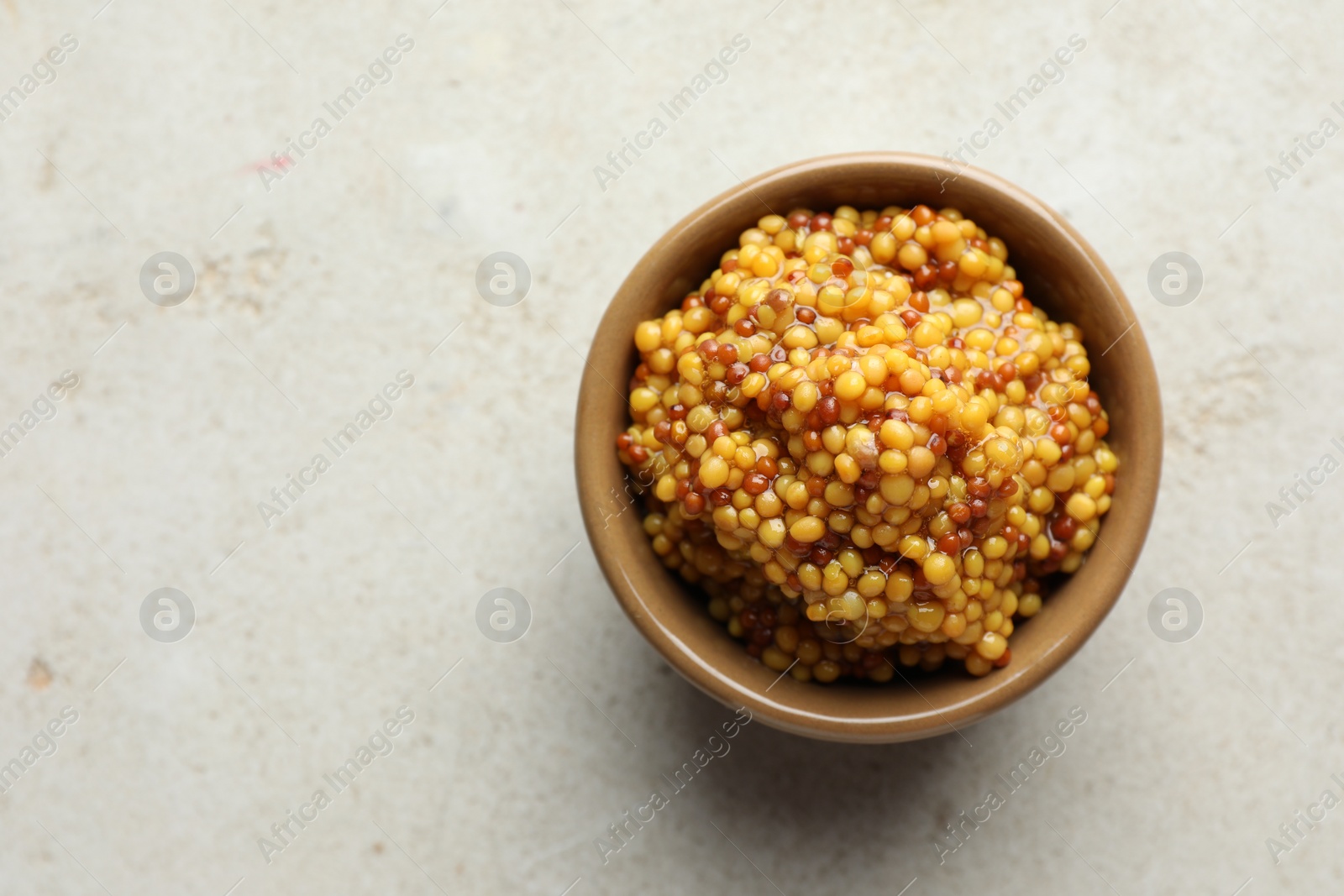 Photo of Whole grain mustard in bowl on light table, top view. Space for text