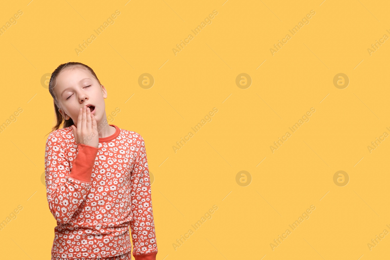 Photo of Sleepy girl yawning on orange background, space for text. Insomnia problem