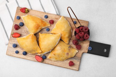 Wooden board with delicious samosas and berries on light table, top view