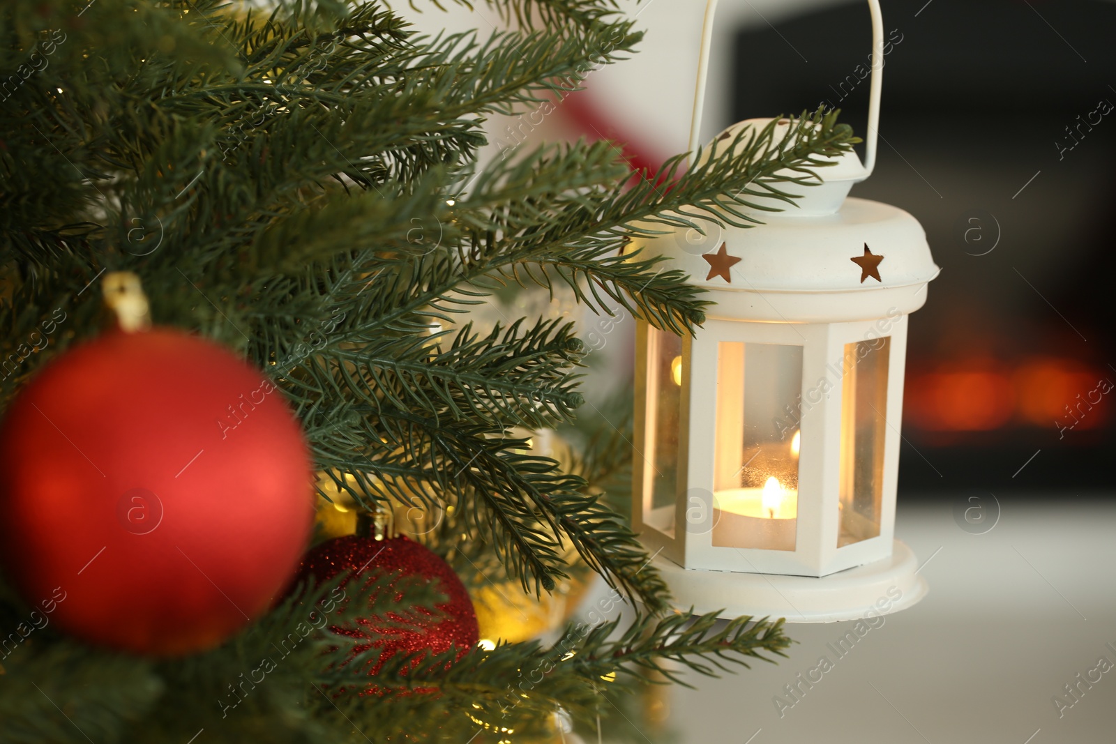 Photo of Christmas lantern with burning candle on fir tree against blurred background, closeup