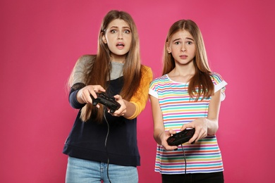 Young woman and teenage girl playing video games with controllers on color background