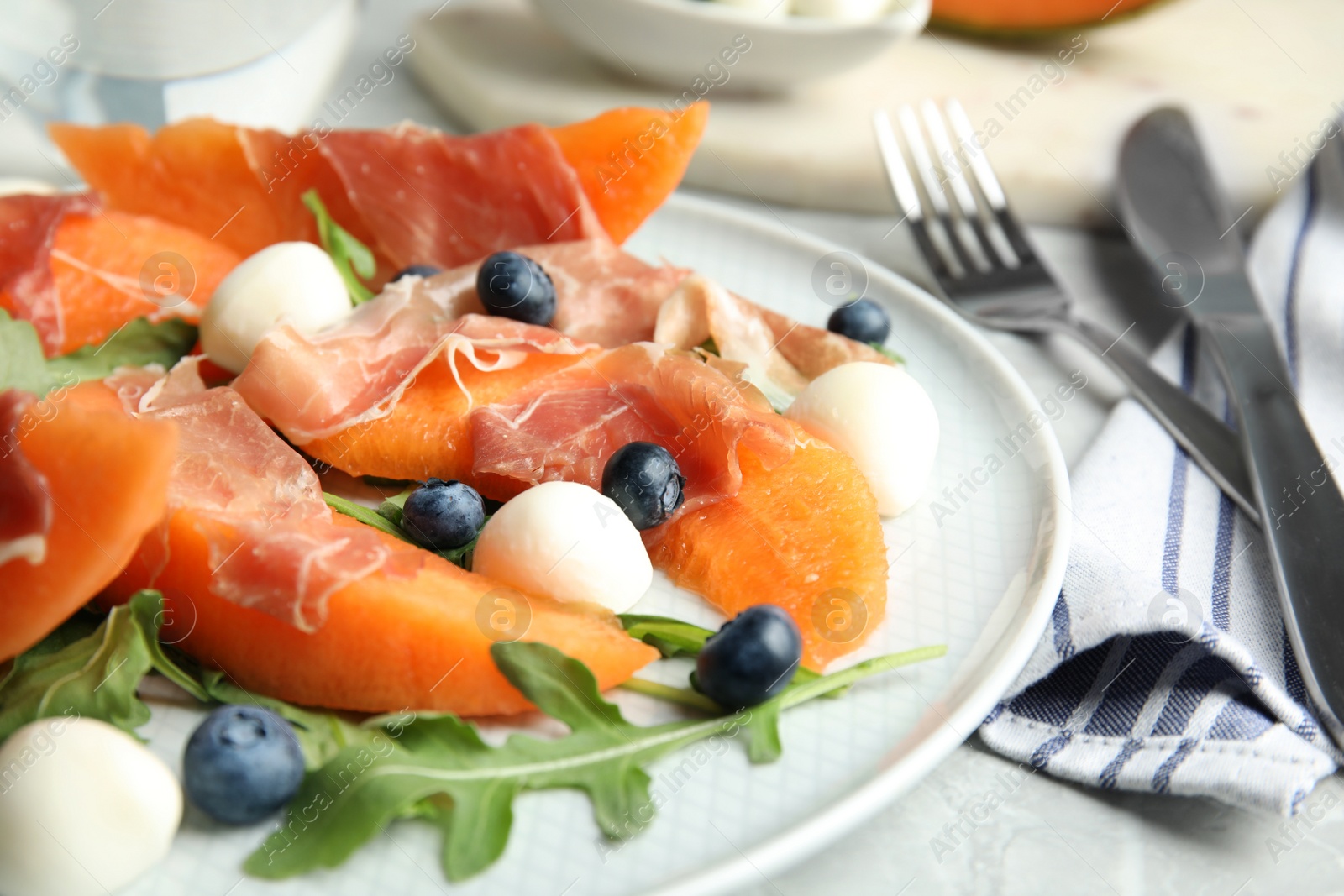 Photo of Fresh melon with prosciutto, mozzarella and arugula on plate, closeup