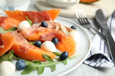 Photo of Fresh melon with prosciutto, mozzarella and arugula on plate, closeup