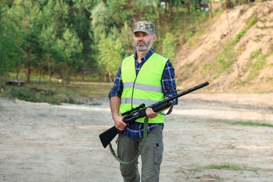 Photo of Man with hunting rifle wearing safety vest outdoors
