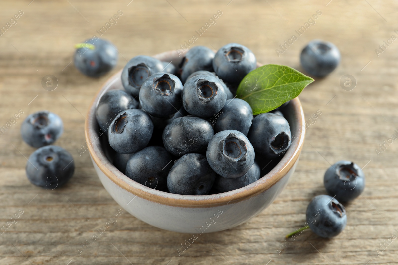 Photo of Bowl of tasty fresh blueberries on wooden table, closeup