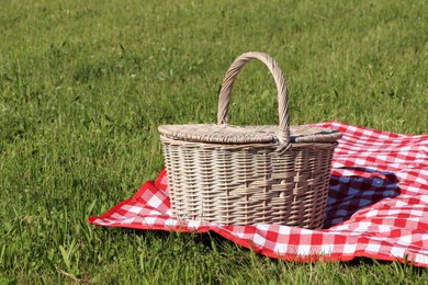 Photo of Picnic basket with checkered tablecloth on green grass outdoors, space for text