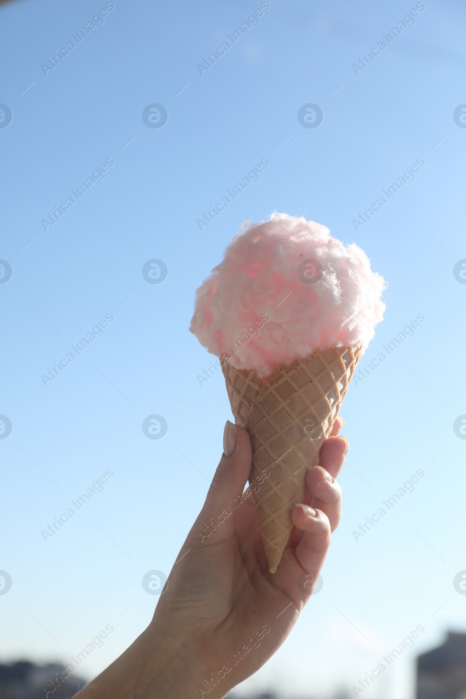 Photo of Woman holding cone with fluffy cotton candy outdoors, closeup