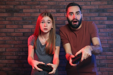 Photo of Young man and teenage girl playing video games with controllers near brick wall