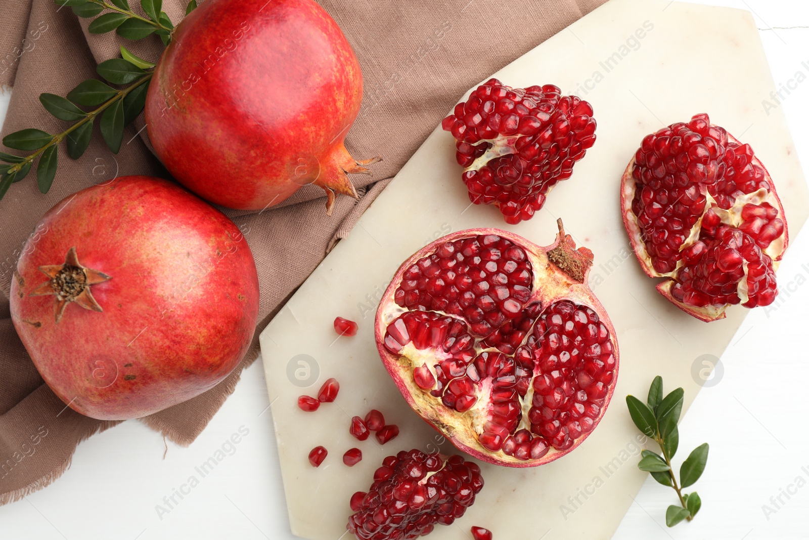 Photo of Fresh pomegranates and branches on white table, flat lay