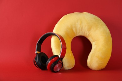 Photo of Yellow travel pillow and headphones on red background, space for text