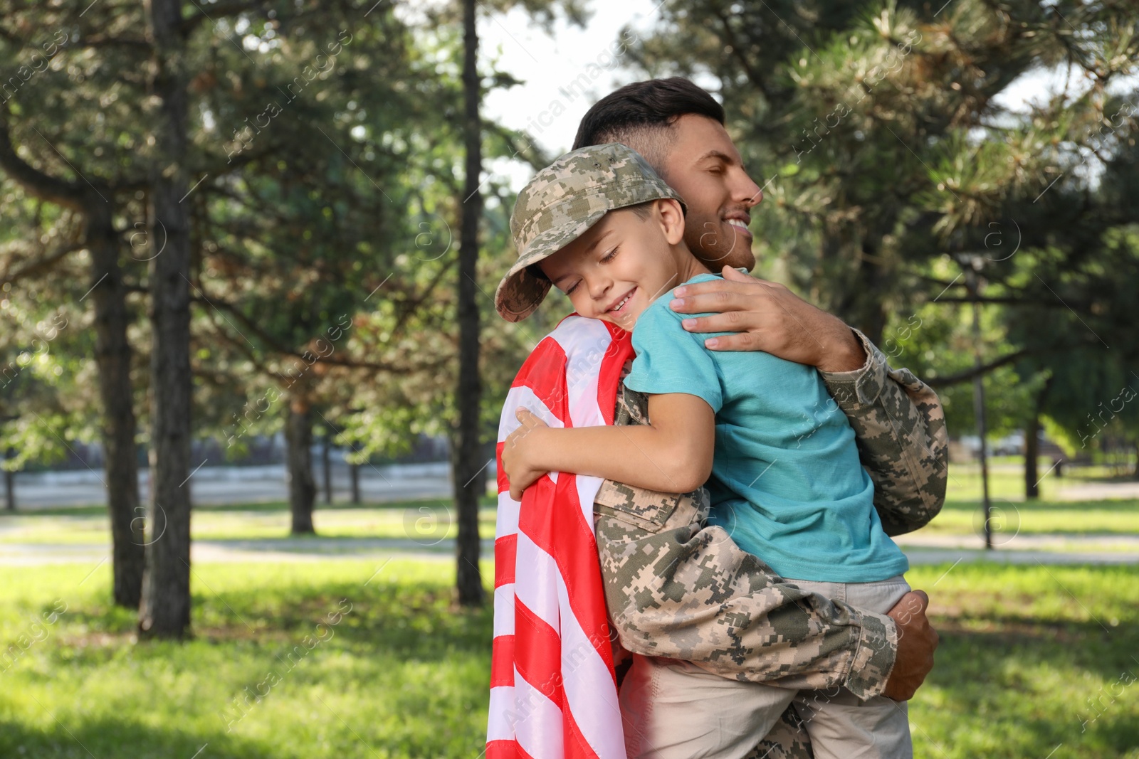 Photo of Soldier with flag of USA and his little son hugging outdoors