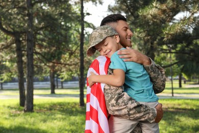 Soldier with flag of USA and his little son hugging outdoors