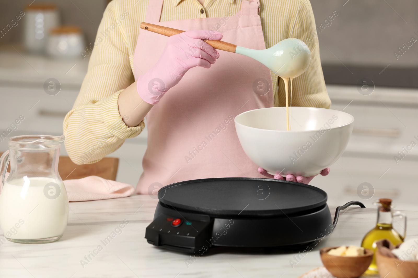 Photo of Woman cooking delicious crepe on electric pancake maker at white marble table in kitchen, closeup