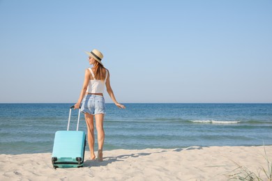 Photo of Woman with suitcase on sandy beach near sea, back view