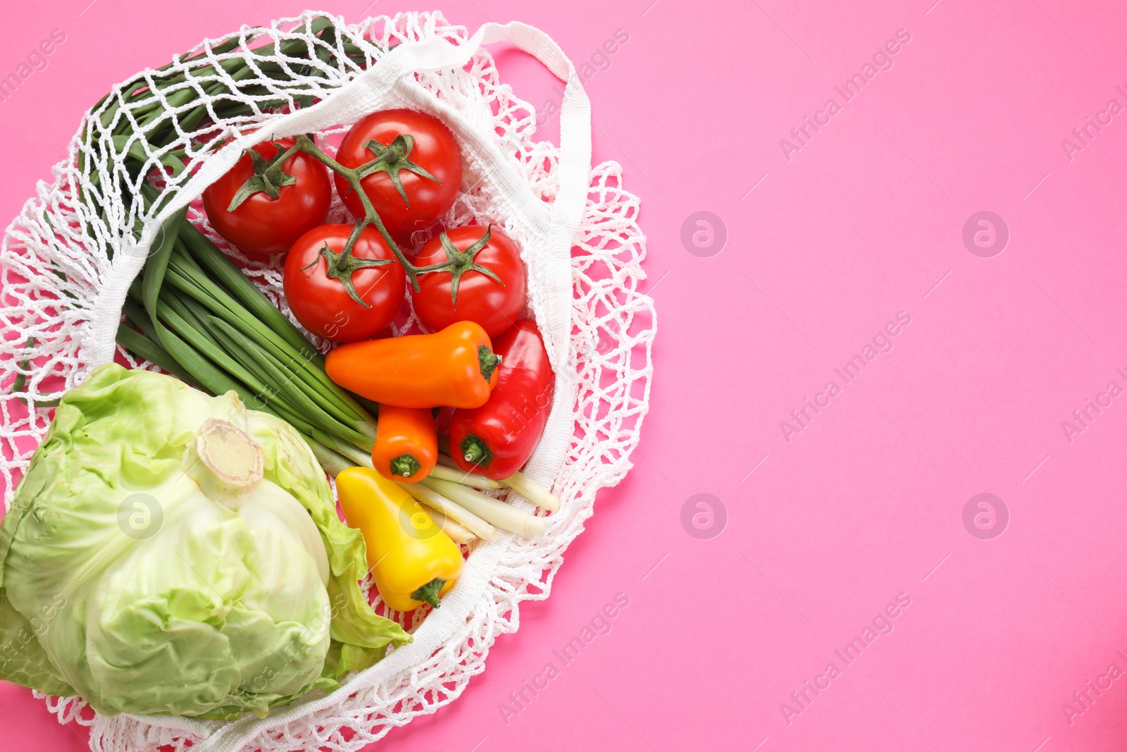 Photo of String bag with different vegetables on bright pink background, top view. Space for text