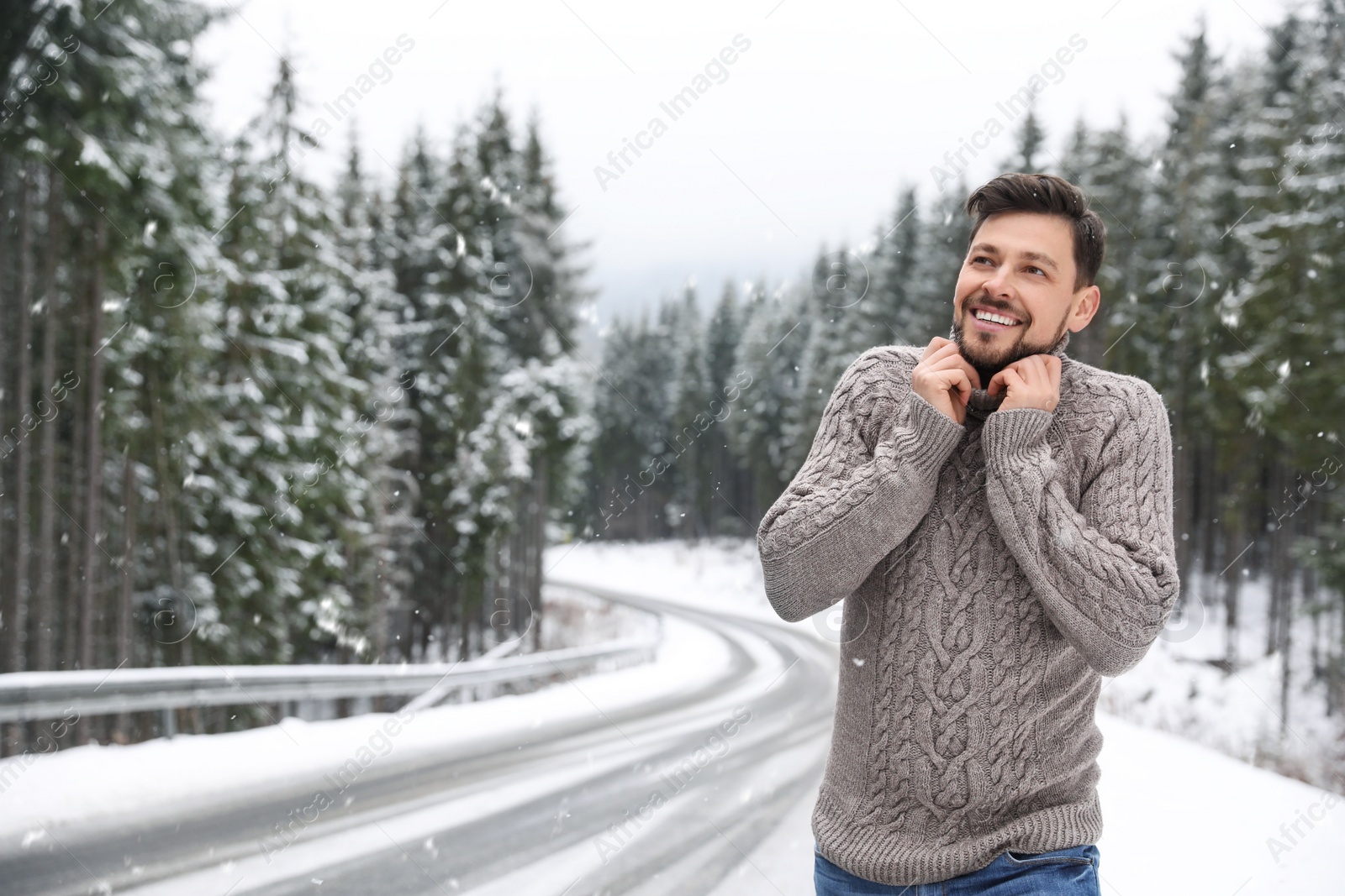 Photo of Man in warm sweater near snowy forest, space for text. Winter vacation