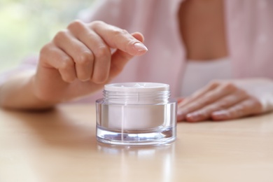 Photo of Woman with jar of moisturizing cream at table, closeup. Space for text