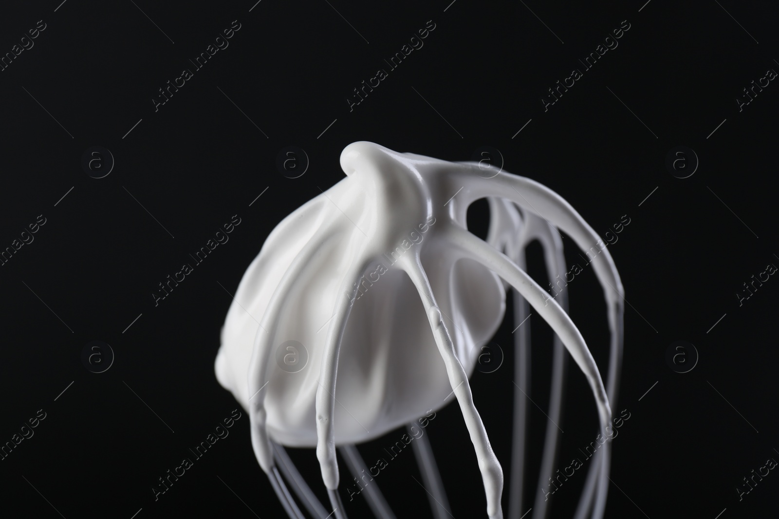 Photo of Whisk with whipped cream on black background, closeup