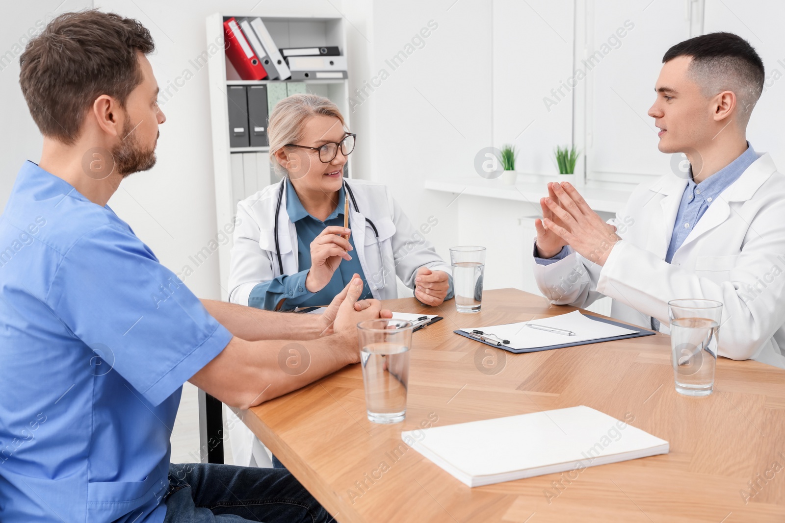 Photo of Medical conference. Team of doctors having discussion at wooden table in clinic