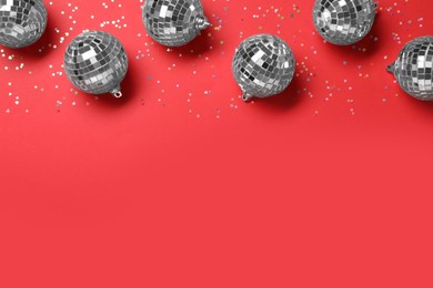 Photo of Shiny disco balls and confetti on red background, flat lay. Space for text