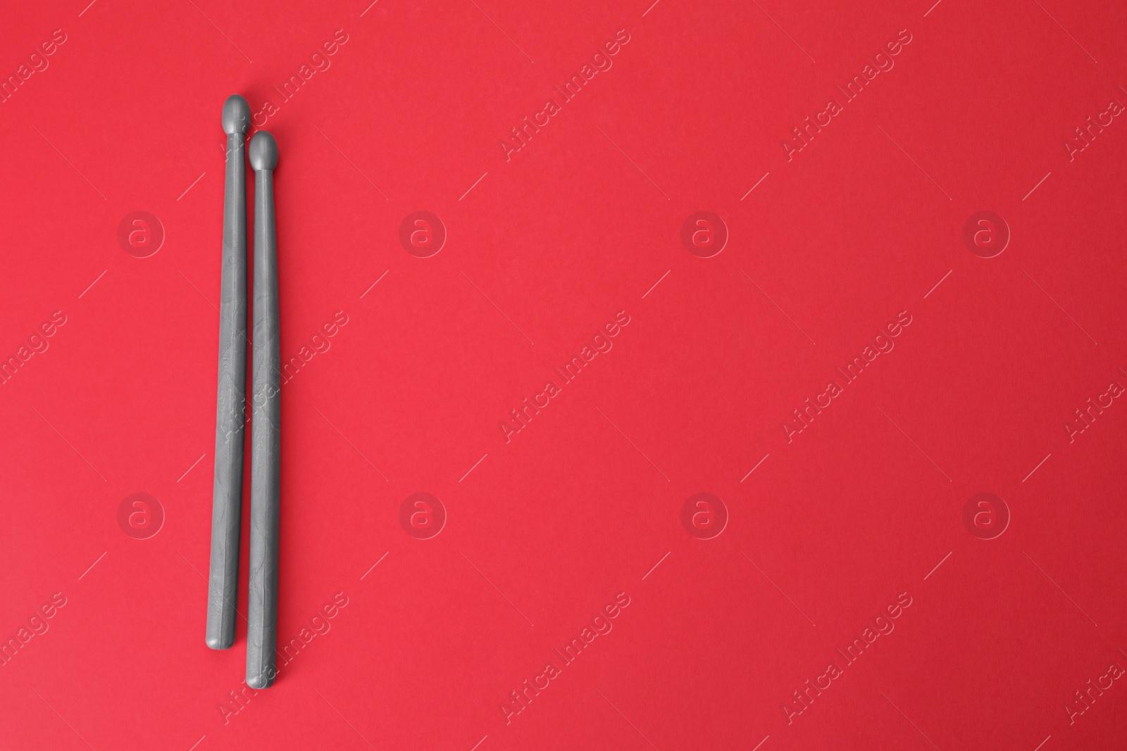 Photo of Two gray drum sticks on red background, top view. Space for text