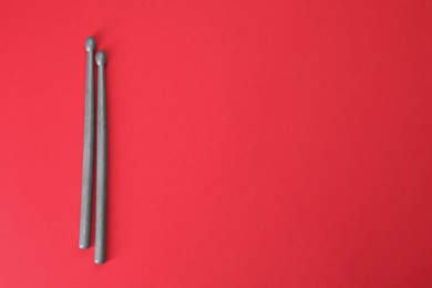 Two gray drum sticks on red background, top view. Space for text