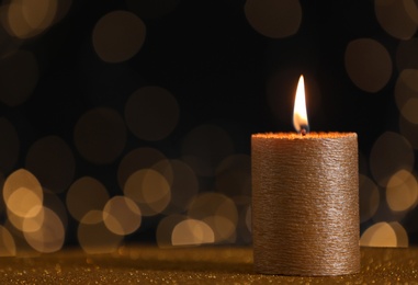 Photo of Burning gold candle on table against blurred lights. Space for text