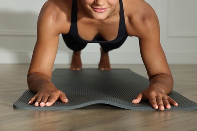 Photo of Young woman doing plank exercise indoors, closeup