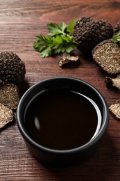 Photo of Fresh truffles and oil in bowl on wooden table