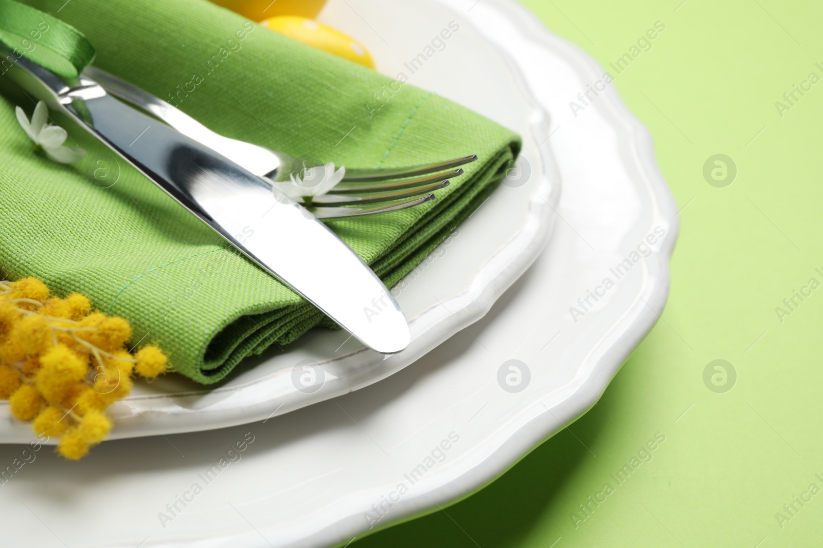 Photo of Festive Easter table setting with floral decor on green background, closeup